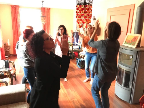 Participants en mouvement lors d'un atelier, dans une pièce chaleureuse aux rideaux orangés.